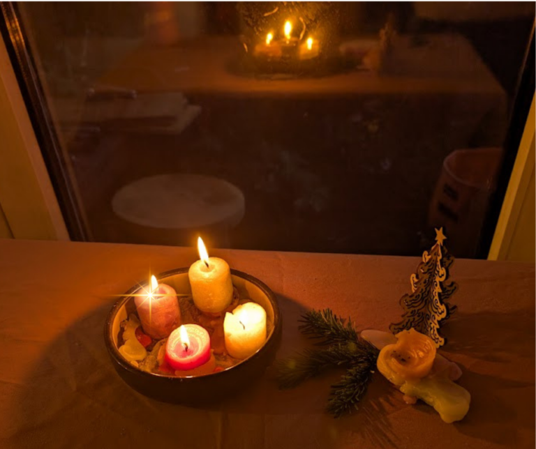 Ein gemütlicher Kerzenteller mit drei brennenden Kerzen auf einer Fensterbank, warmes Licht, daneben Tannenzweig und kleine Weihnachtsdeko.
