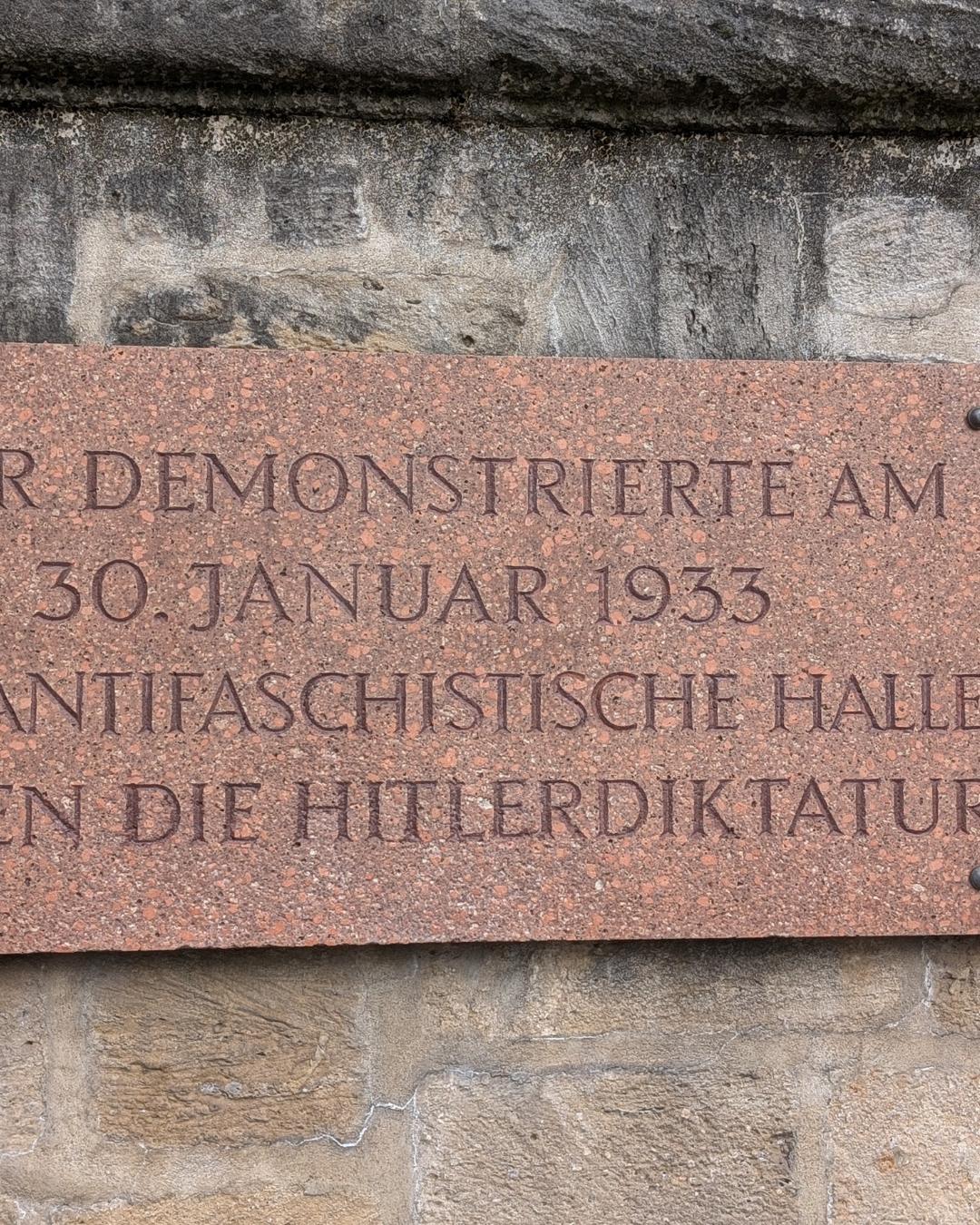 Nahaufnahme einer rötlichen Gedenktafel aus Granit am Roten Turm in Halle (Saale) mit einer Inschrift zum antifaschistischen Widerstand am 30. Januar 1933.