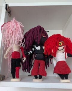 Drei Amigurumi-Dolls in unterschiedlichen Entstehungsphasen: Von der bloßen gehäkelten Körperform über eine teil-eingekleidete Figur bis hin zum fertigen Charakter mit Gesichtsausdruck und Frisur