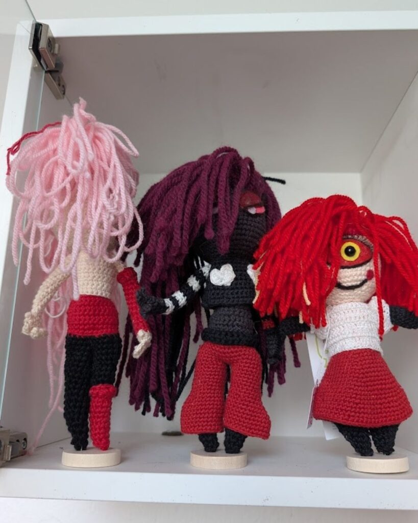 Drei Amigurumi-Dolls in unterschiedlichen Entstehungsphasen: Von der bloßen gehäkelten Körperform über eine teil-eingekleidete Figur bis hin zum fertigen Charakter mit Gesichtsausdruck und Frisur